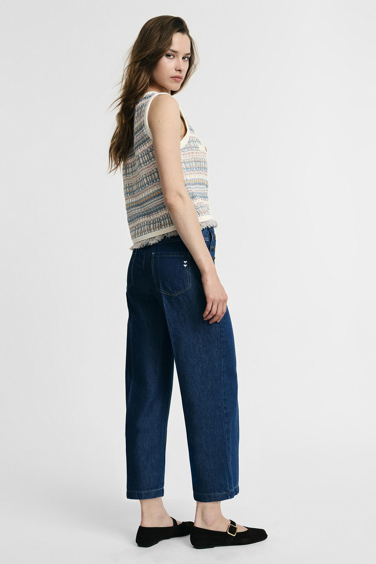 Woman modelling dark blue wide-leg cropped women's jeans with knitted sleeveless top and black buckle flats, standing and looking back