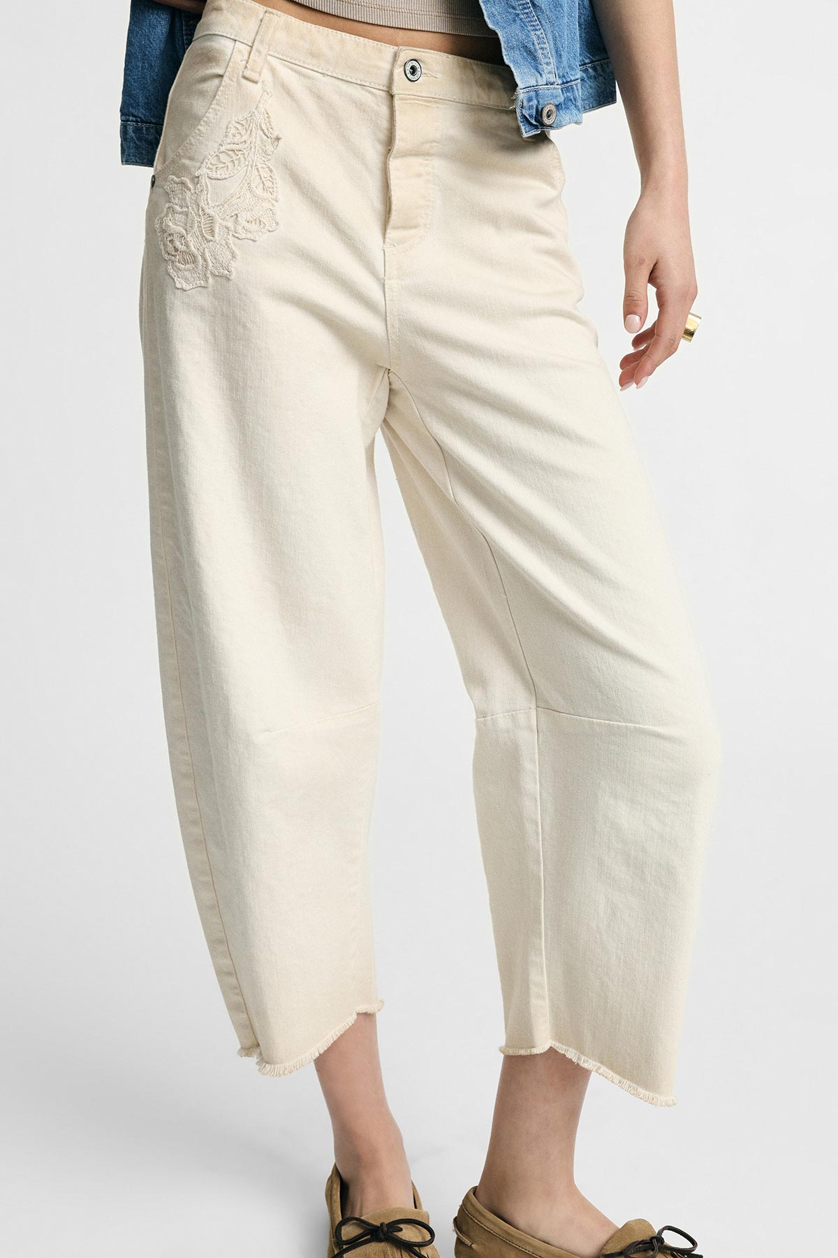 Cream cropped wide-leg trousers with embroidered floral detail and frayed hem, styled with denim jacket and lace-up shoes