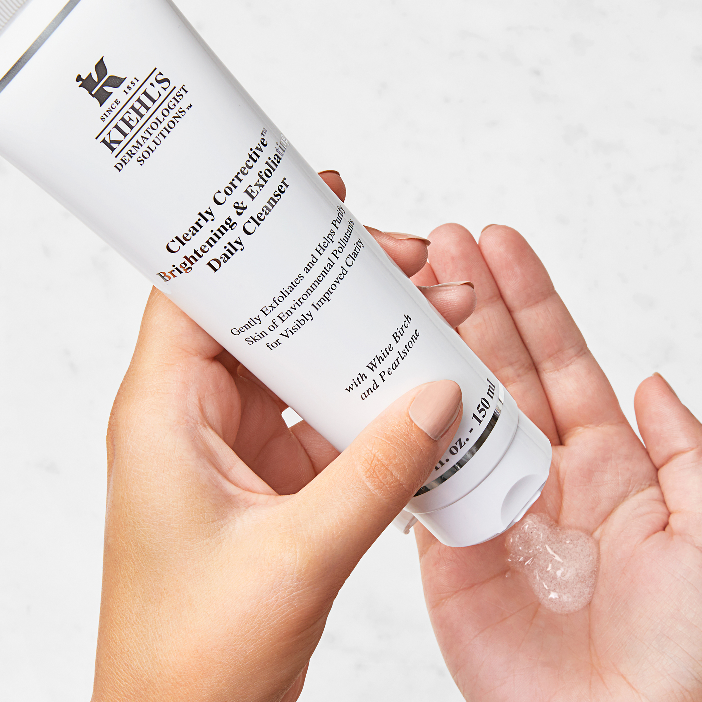 Mano che tiene il tubetto bianco del Kiehl's Clearly Corrective Brightening & Exfoliating Daily Cleanser