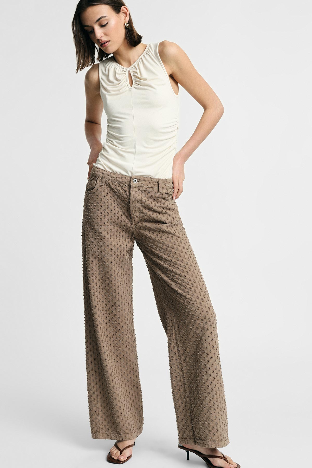 Woman modelling cream ruched sleeveless top with keyhole paired with high‑waist textured wide‑leg brown trousers and sandals