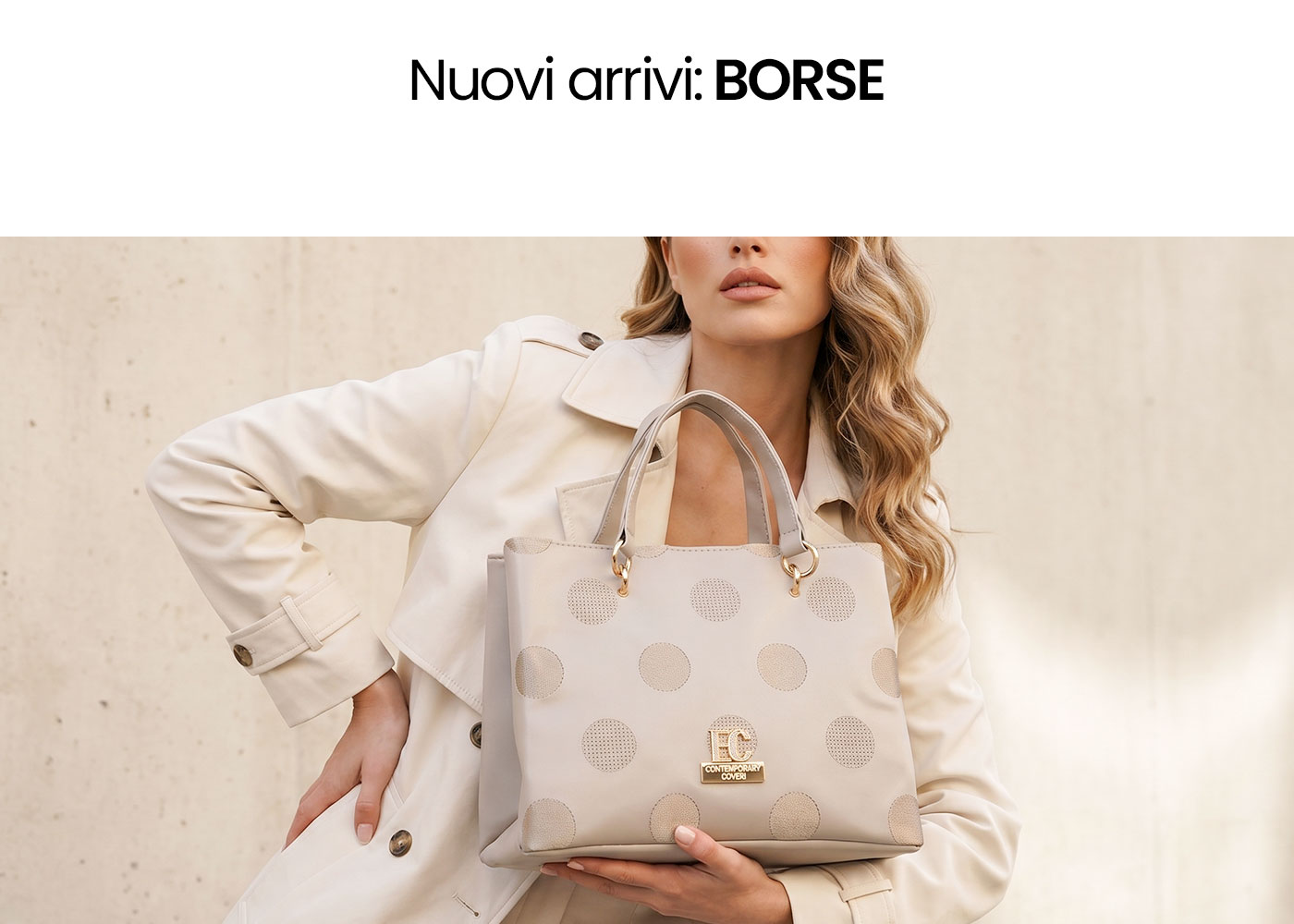 Woman holding beige polka-dot tote handbag with gold logo, wearing cream trench coat against a neutral background