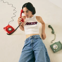 Donna in top corto bianco e jeans sdraiata sul pavimento, con in mano un telefono a rotella rosso, e accanto a lei un telefono a rotella verde.