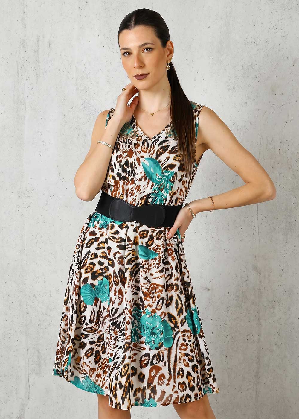 Woman modelling sleeveless leopard-print dress with turquoise floral accents and wide black belt, standing against a concrete wall