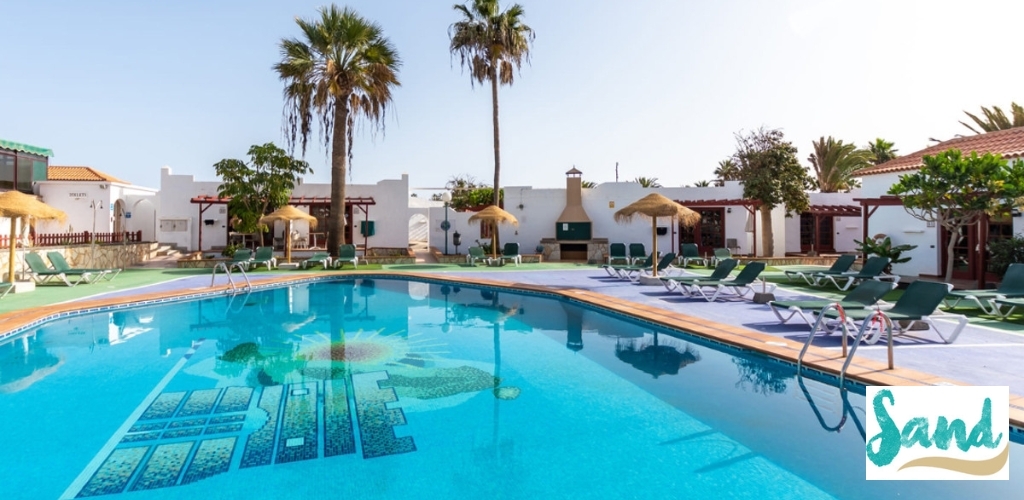 Resort swimming pool with mosaic turtle tile, sun loungers and thatched parasols, palm trees and white villas under a clear blue sky