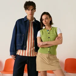 Giovane uomo e donna in piedi davanti a sedie arancioni, indossano abiti casual primaverili con sneakers, sfondo neutro.
