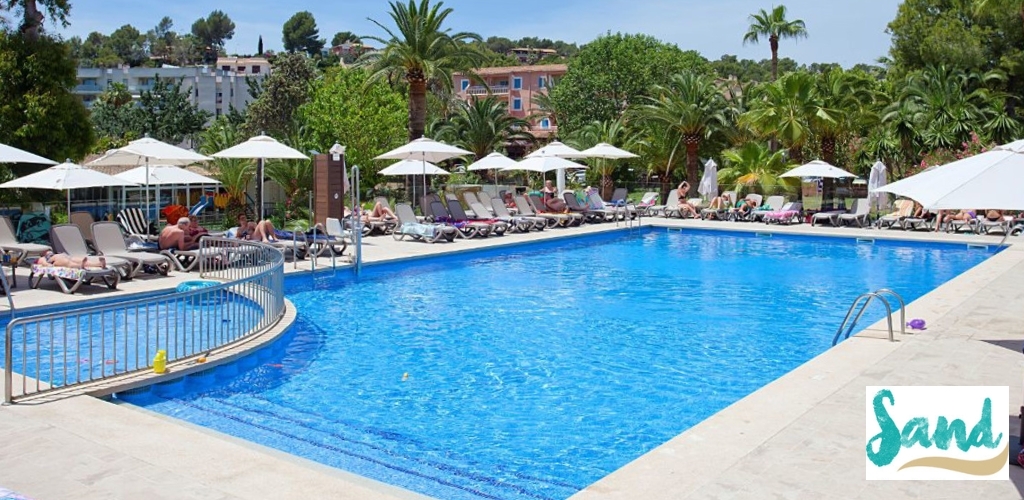 Hotel outdoor pool with clear blue water, sunloungers, umbrellas and palm trees, guests relaxing on the poolside
