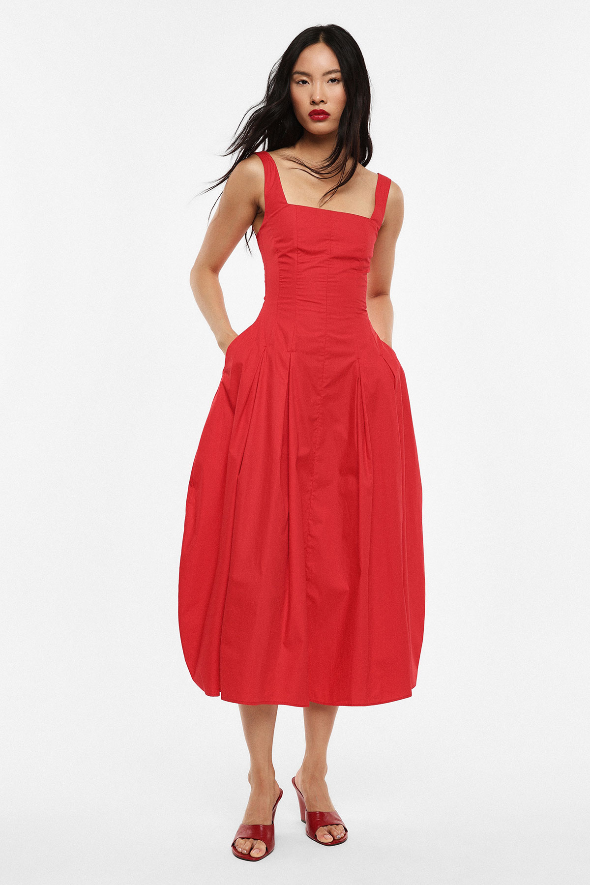 Model wearing a red midi dress with square neckline and side pockets, paired with red heeled sandals on a white background
