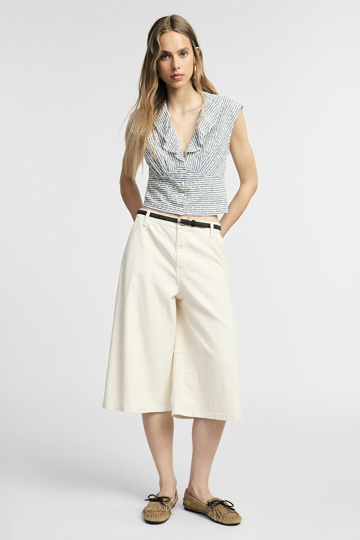 Full-length woman in striped sleeveless V-neck top, cream wide culotte trousers with black belt and moccasin shoes