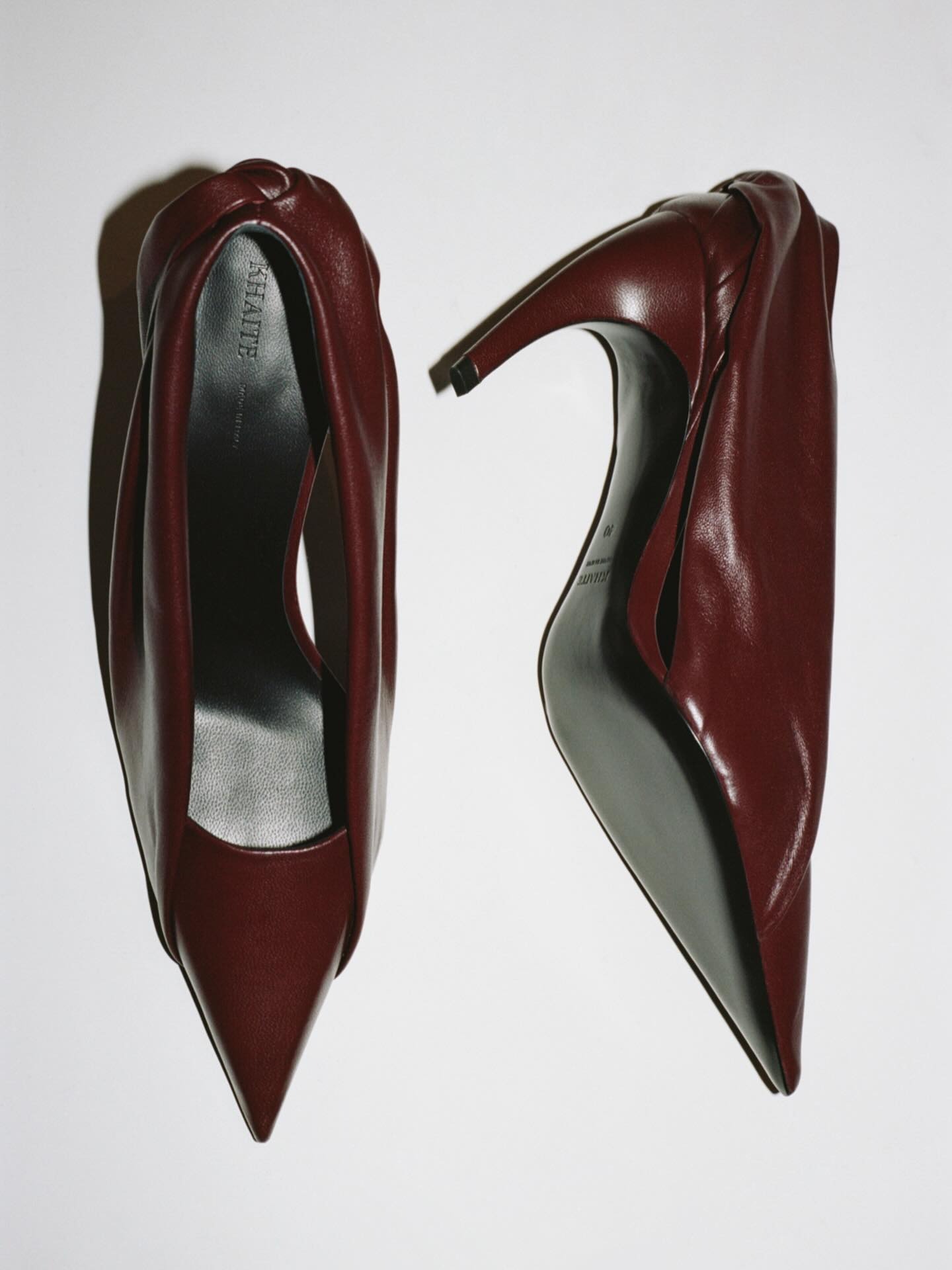Pair of burgundy leather pointed-toe high-heeled women's shoes on white background, top view