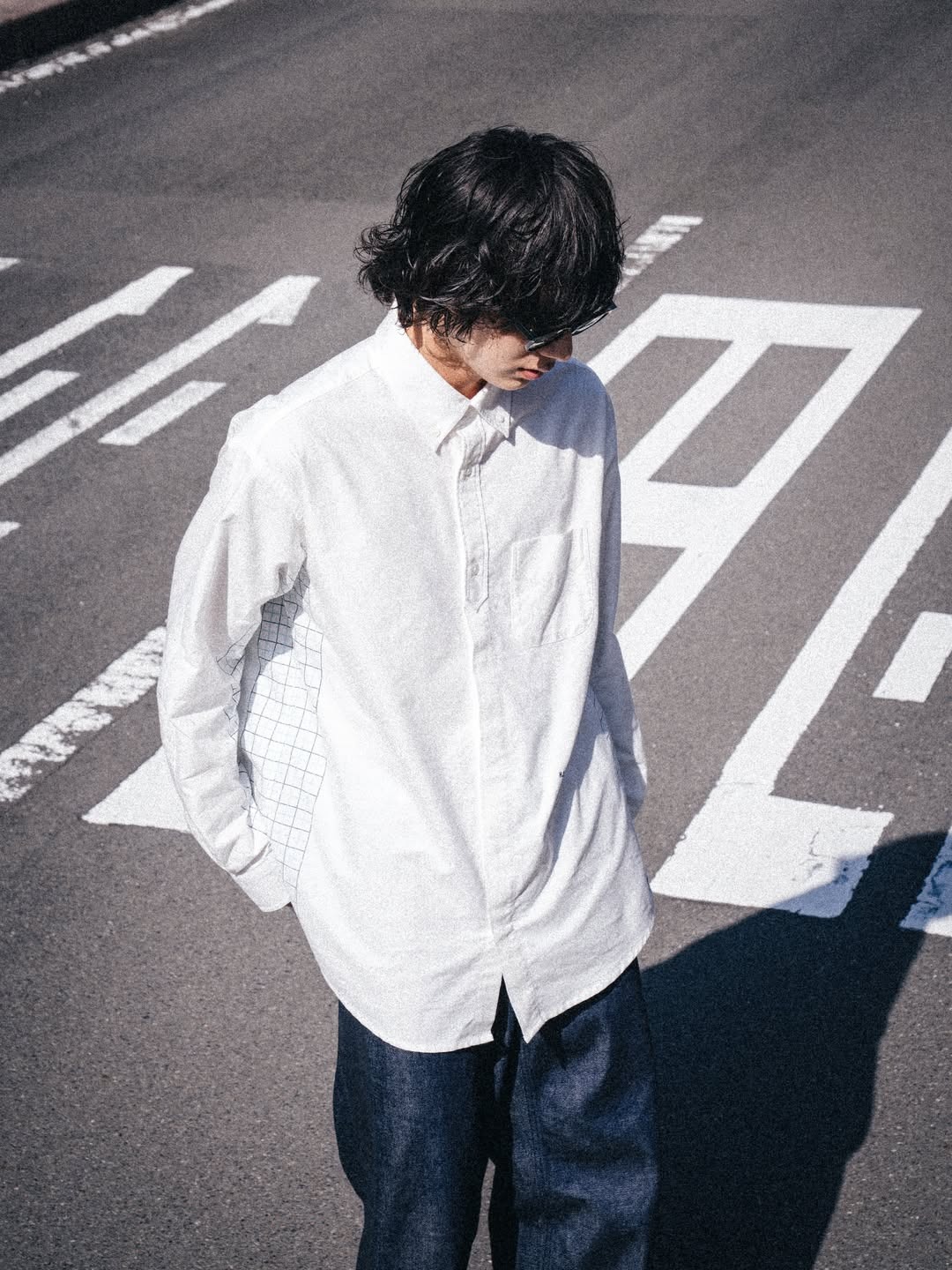 Young person in white shirt and dark trousers standing on road markings, looking down with hands in pockets