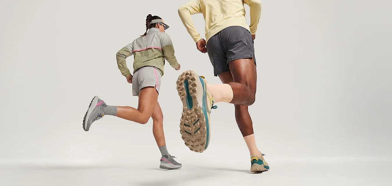 Due persone con abbigliamento sportivo e cappellini che corrono verso avanti su uno sfondo chiaro e uniforme.