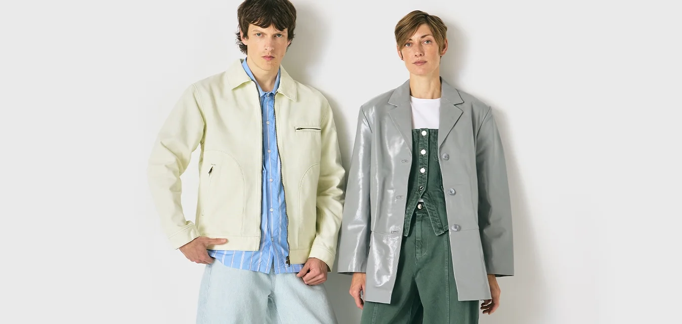 Due modelle si trovano davanti a uno sfondo bianco, indossando giacche casual di grandezza oversize, una crema su una camicia blu e l'altra grigia su un outfit verde.