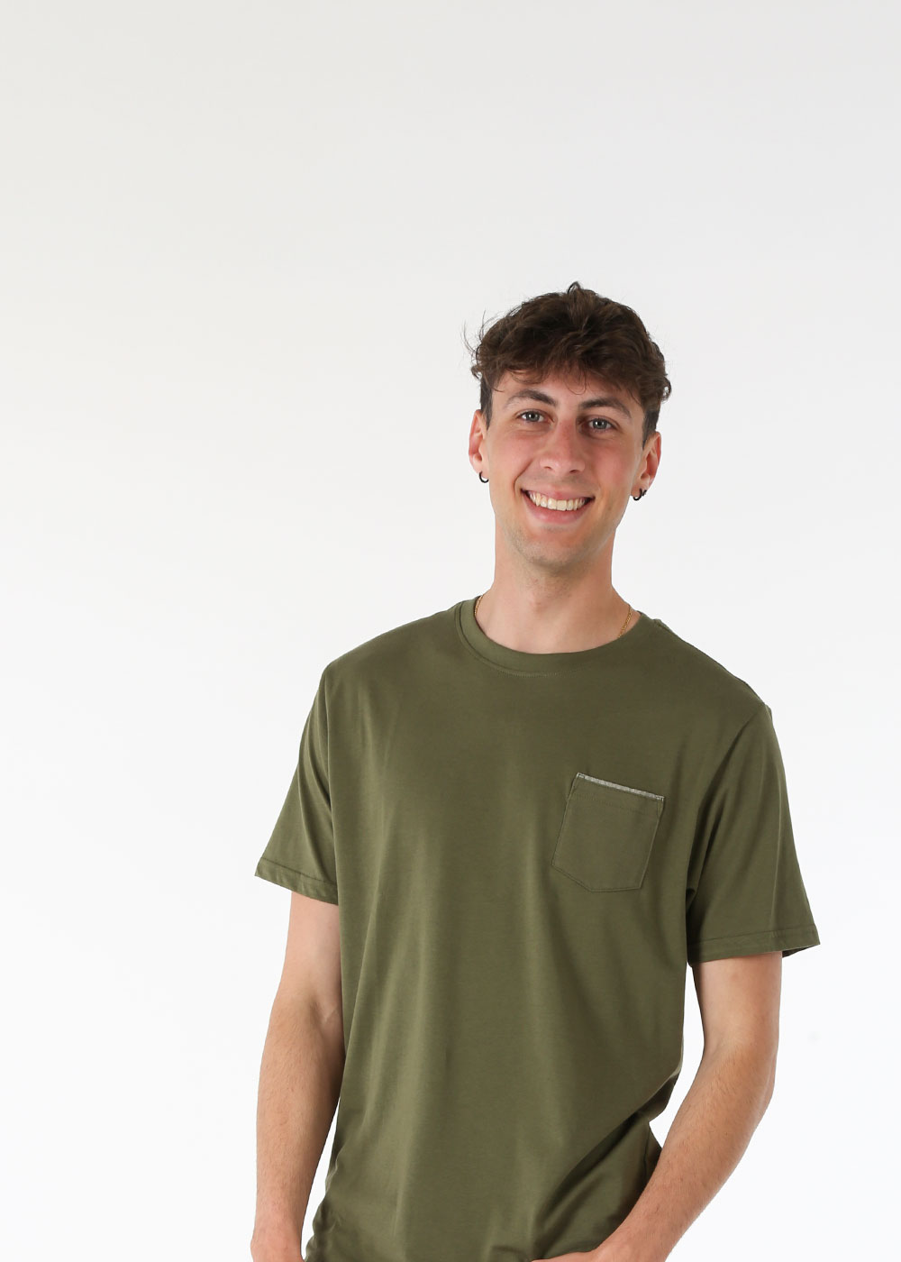 Smiling young man wearing an olive-green pocket T-shirt standing against a plain white background