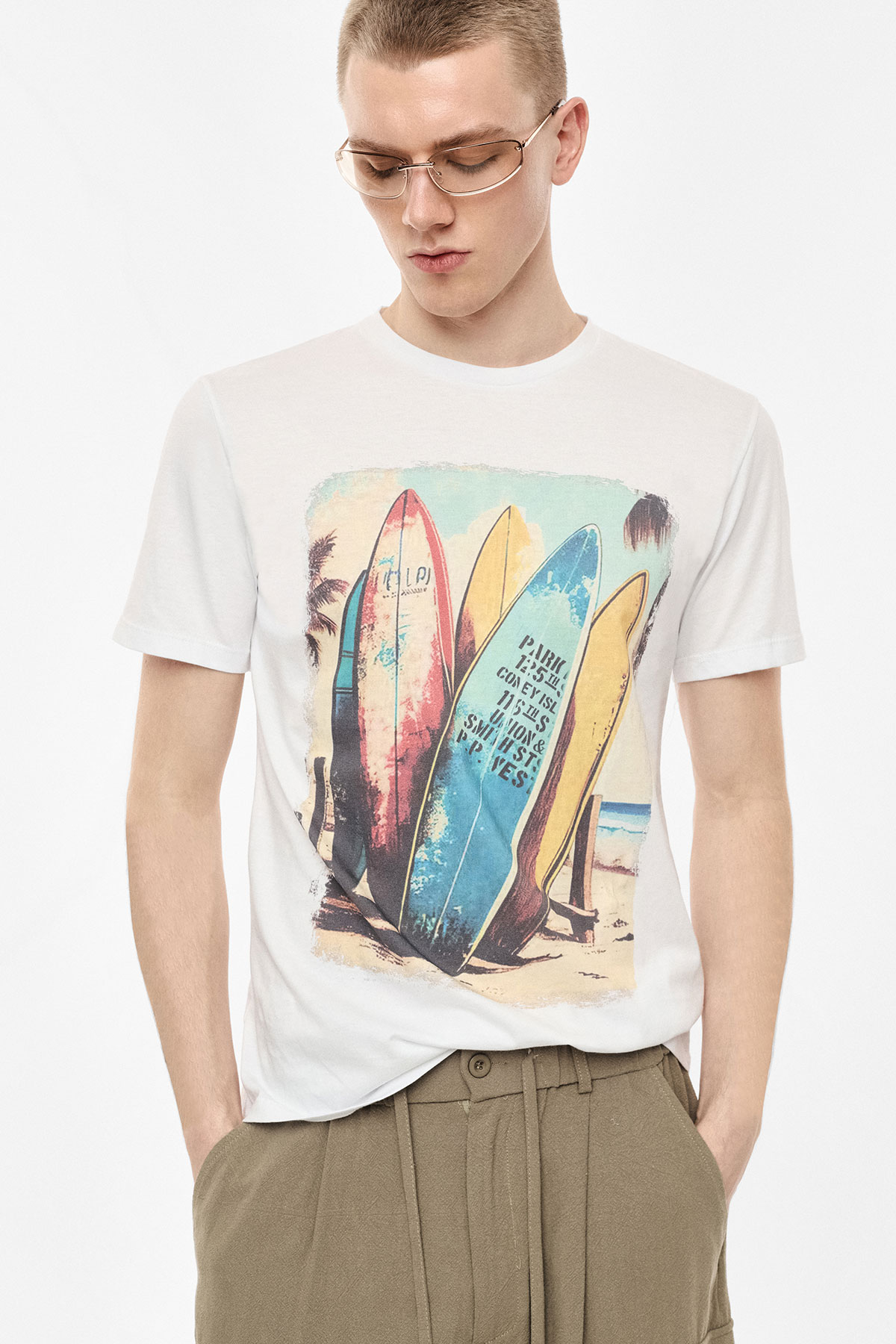 Young man wearing white T-shirt with colourful vintage surfboard graphic and khaki trousers