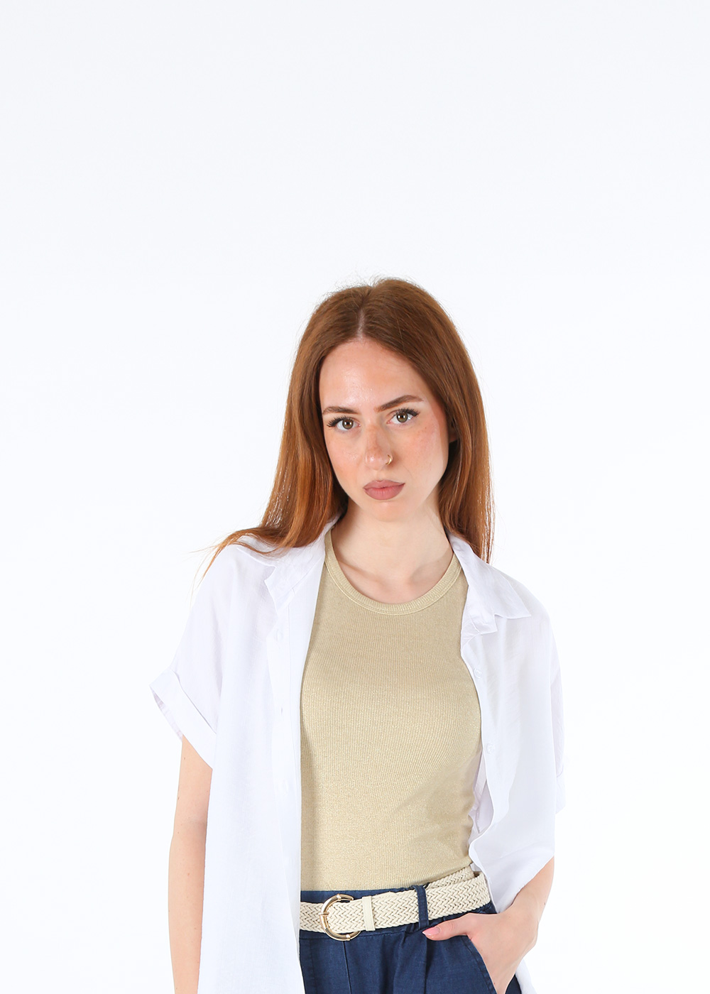 Young red-haired woman model in white short-sleeve shirt, beige ribbed top and woven belt, hand in pocket studio portrait