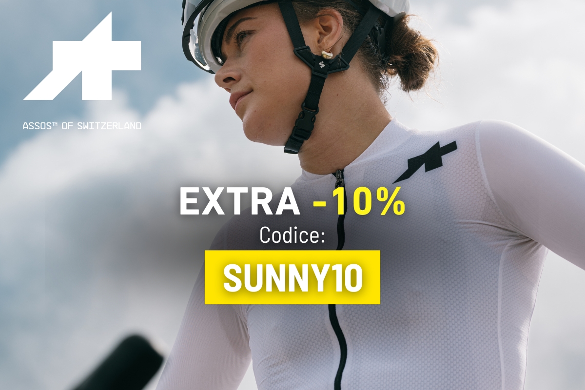 Close-up of a cyclist in white Assos cycling kit and helmet with promotional text "EXTRA -10% Code: SUNNY10" over a cloudy sky