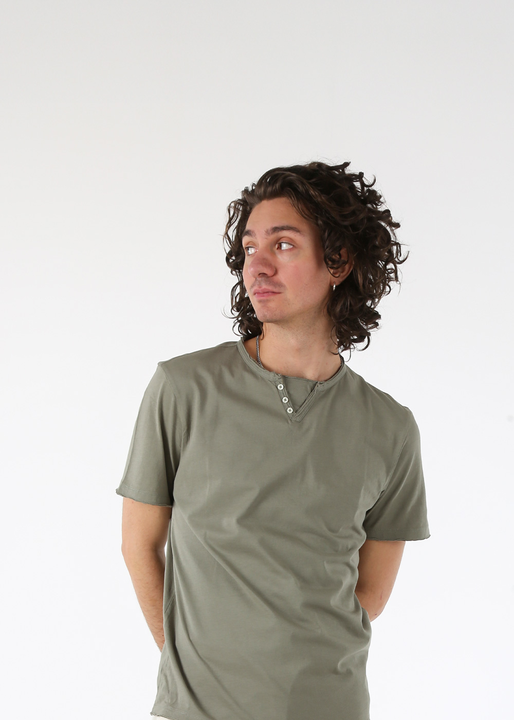 Young man in olive-green short-sleeve henley T-shirt looking sideways in a casual fashion pose against plain white background