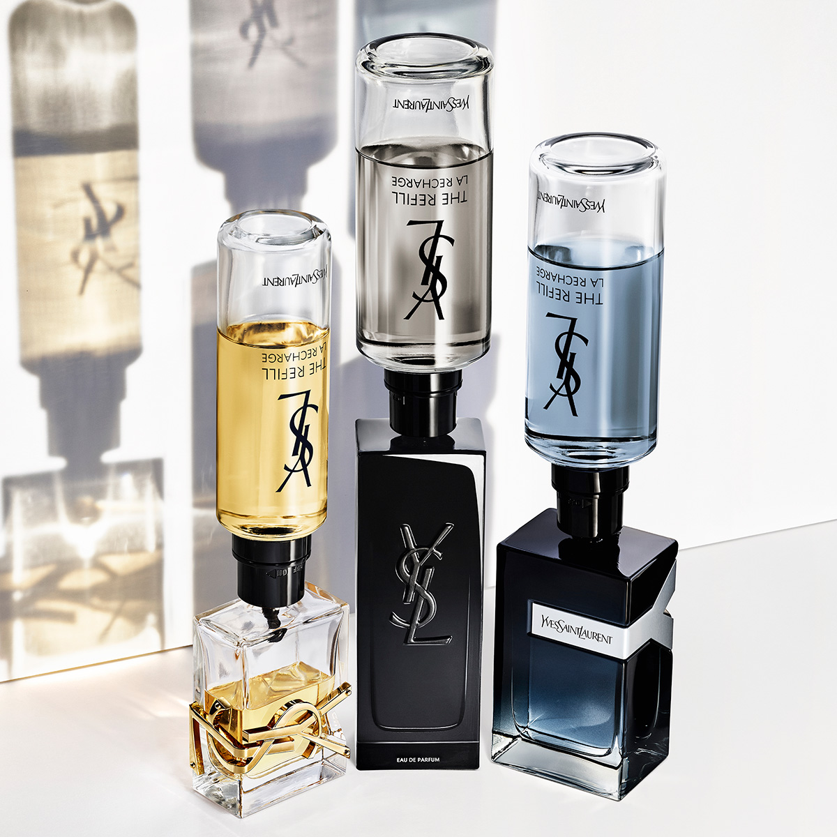 Tre diversi flaconi di profumo YSL &mdash; Libre, MYSLF e Y &mdash; ricaricati contemporaneamente con i loro flaconi di ricarica capovolti.