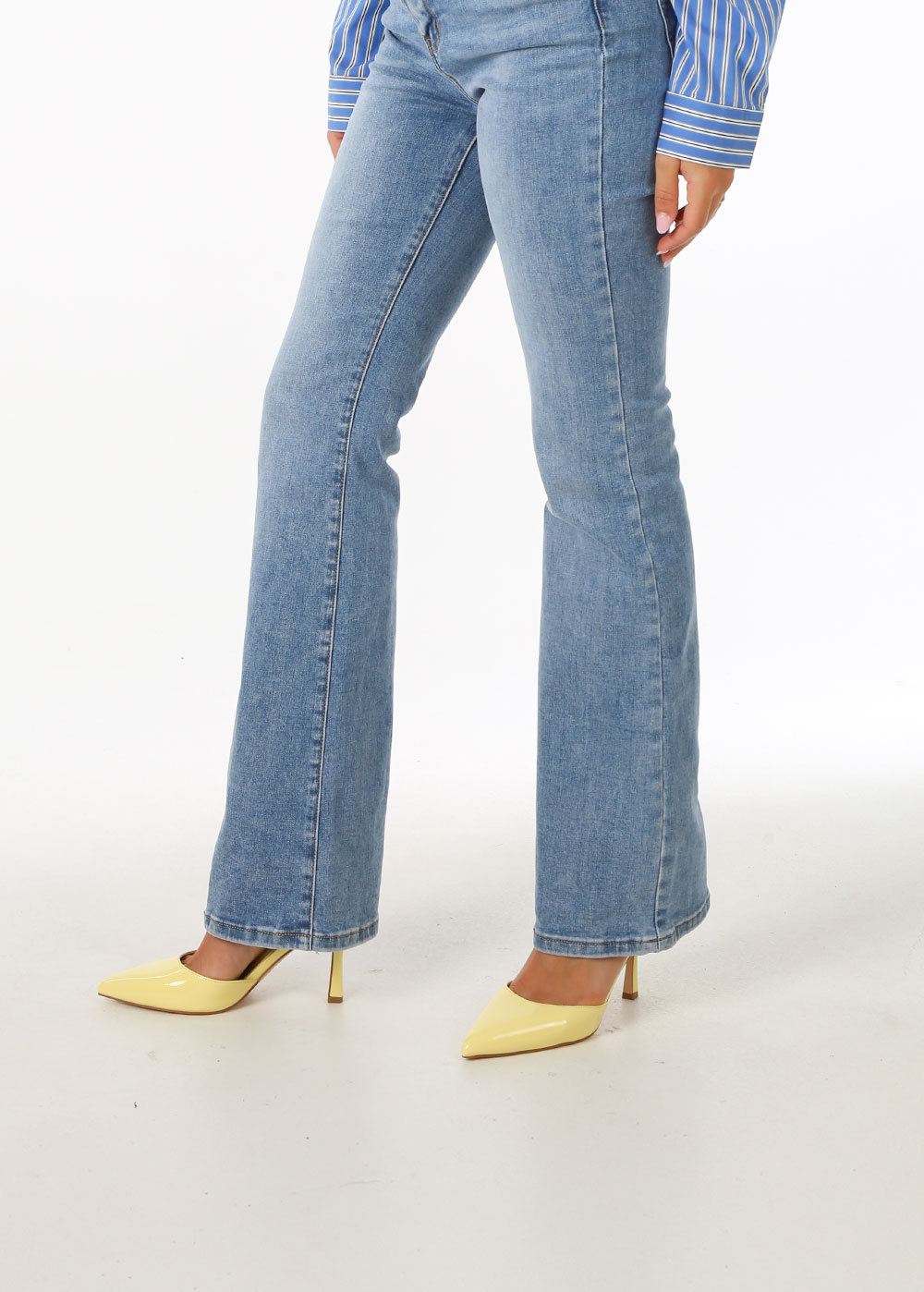 Model wearing light-blue bootcut jeans and yellow pointed high-heeled pumps on white background