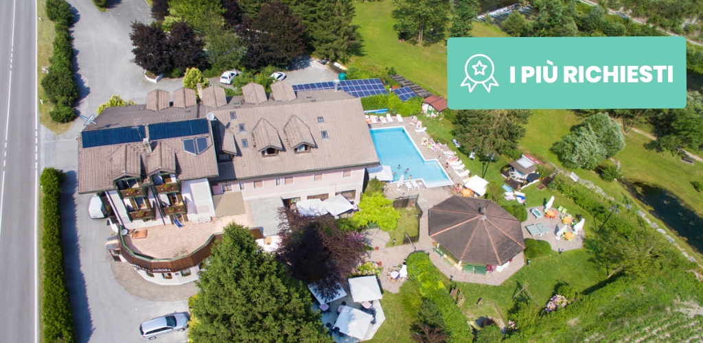 Aerial view of countryside hotel and outdoor swimming pool surrounded by gardens, trees, solar panels and adjacent road