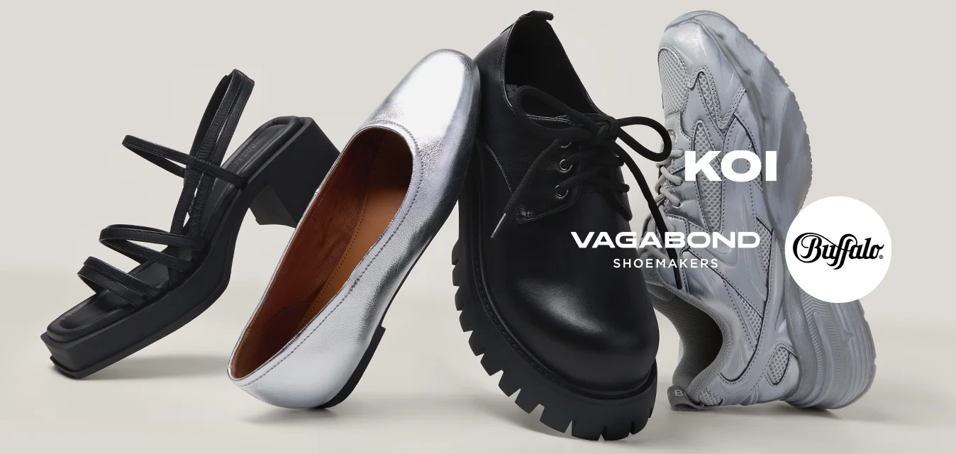 Quattro scarpe singole in piedi in fila, tra cui un sandalo nero, una scarpa piatta argento, una scarpa nera chunky e una sneaker bianca su una superficie bianca.