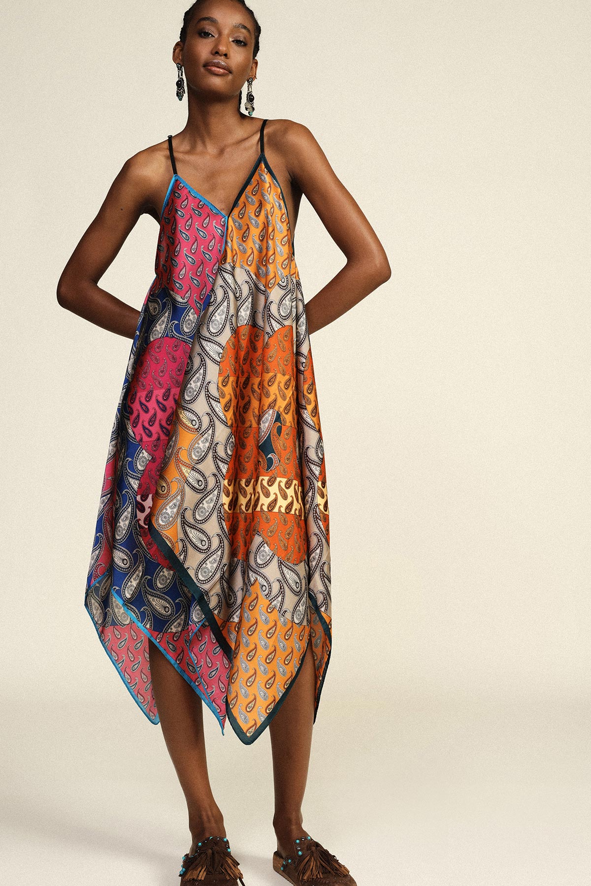 Woman wearing colourful patchwork paisley handkerchief-hem sundress with thin straps and tassel sandals