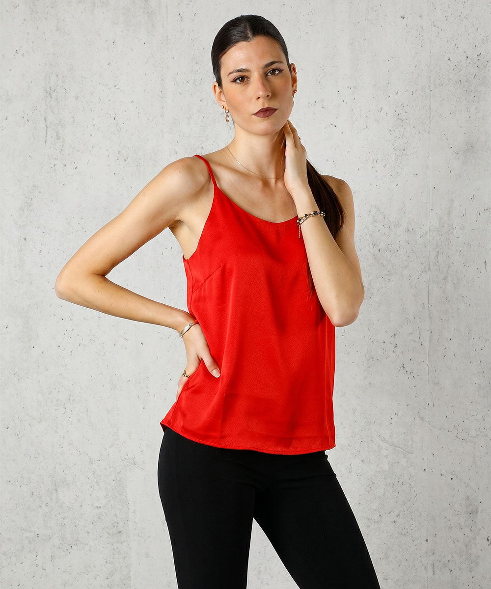 Woman wearing red camisole top and black trousers posing against a light concrete wall