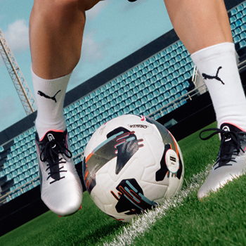 Close-up of footballer’s legs in silver boots and white Puma socks controlling a football on a stadium pitch