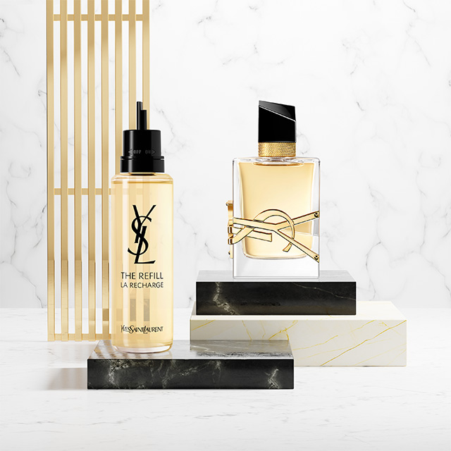 Un flacone di profumo YSL Libre e la sua ricarica dorata esposti su piedistalli in marmo e pietra nera.