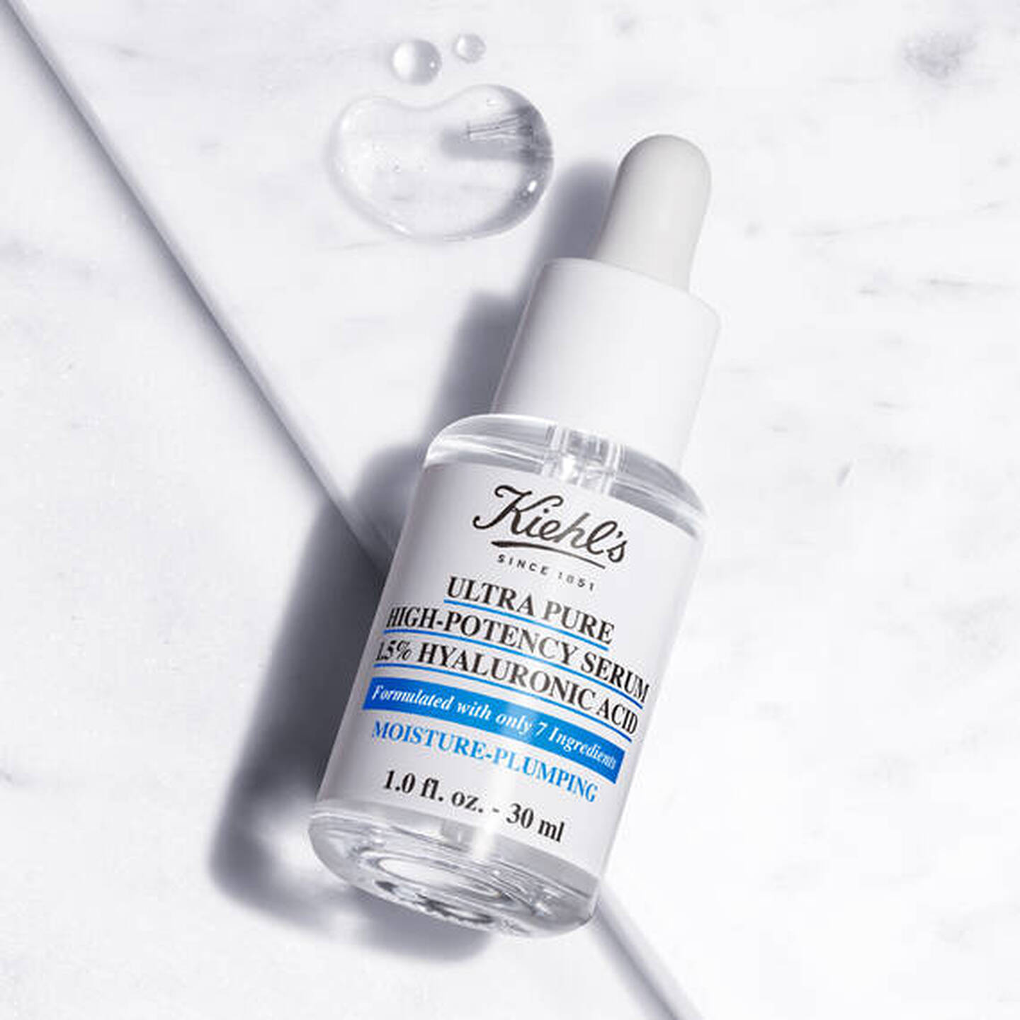 Flacone di Ultra Pure High-Potency Serum 1,5% Hyaluronic Acid Kiehl's su superficie marmorea con gocce di siero.
