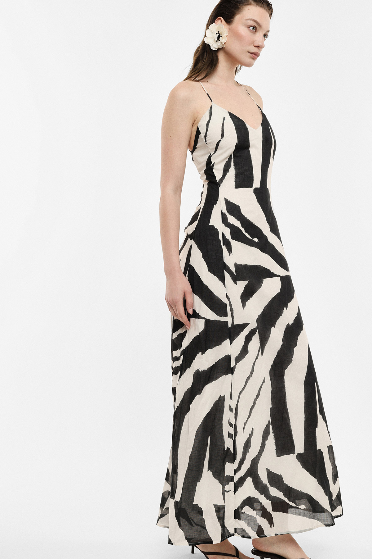 Woman wearing a black-and-white zebra print maxi dress with thin straps and a flower hair clip, side profile on white background