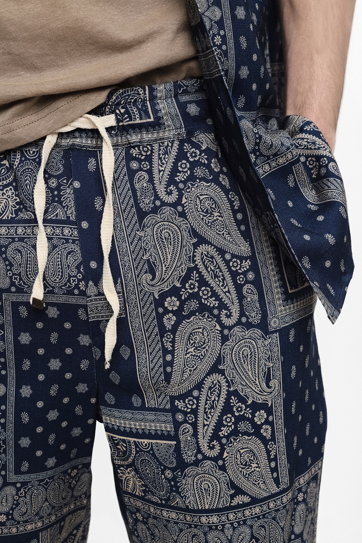 Close-up of navy paisley-print drawstring trousers and matching jacket, hand in pocket with beige top visible