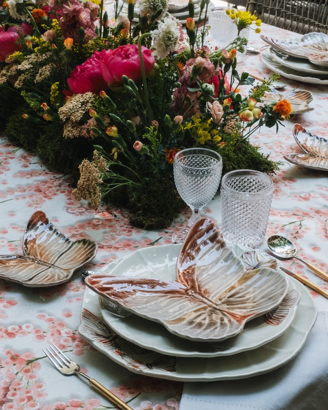 Elegant spring table setting with butterfly-shaped plates, textured glassware, cutlery and floral centerpiece on a patterned tablecloth