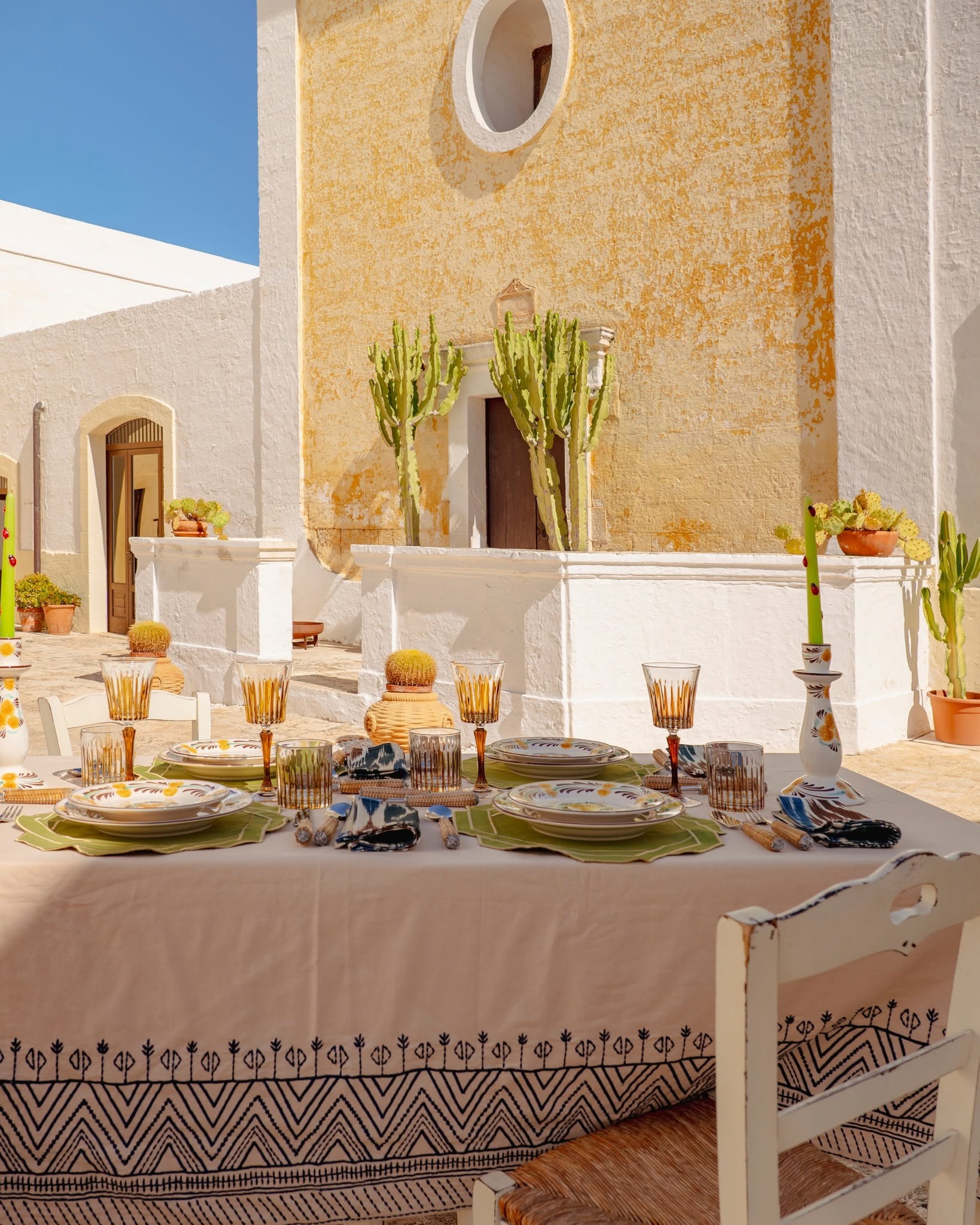 Al fresco courtyard dining set with colourful plates, amber glassware and cacti against a sunlit yellow wall