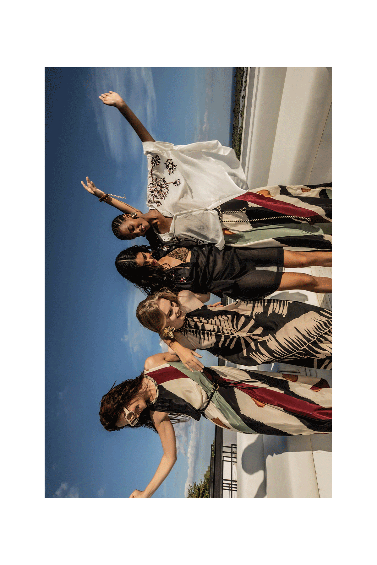 Group of diverse women in patterned summer dresses celebrating with balloons on a sunlit seaside terrace