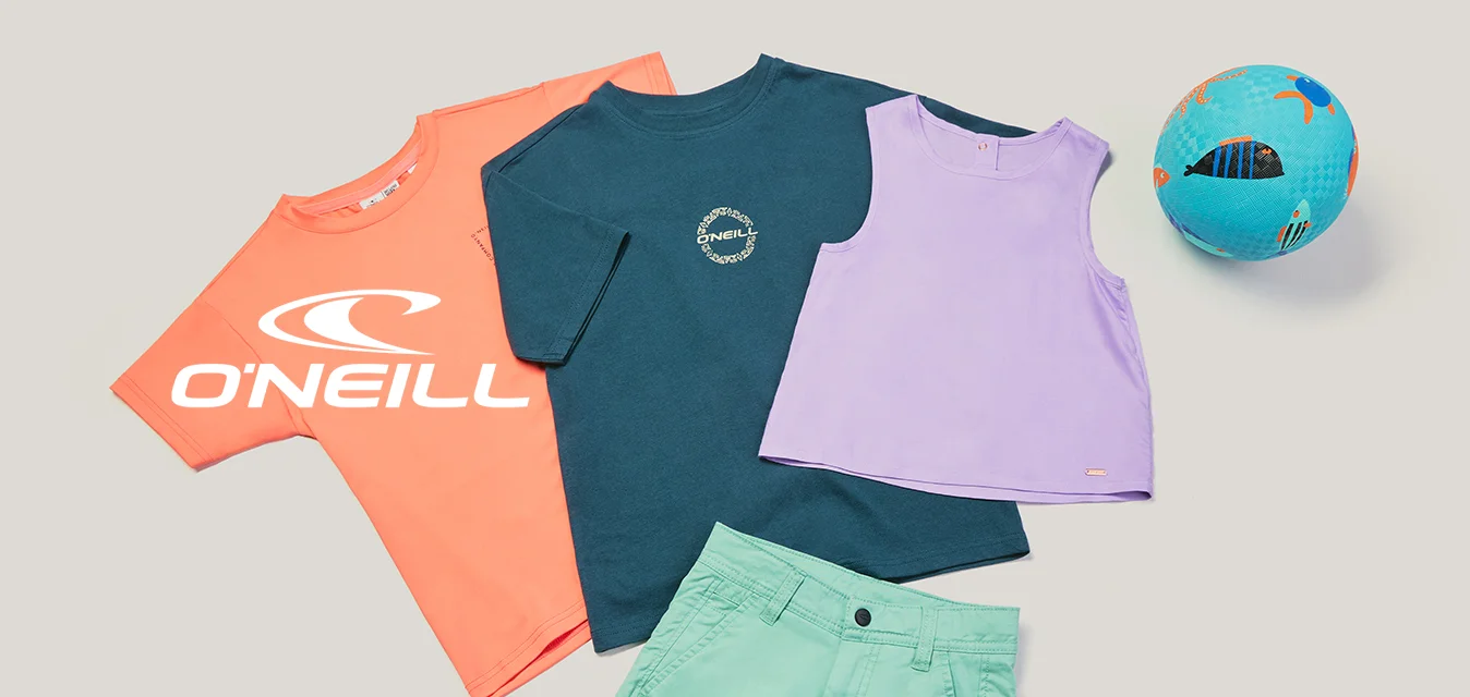 Tre t-shirt colorate, pantaloncini verdi e un pallone da calcio blu disposti su uno sfondo chiaro e uniforme.