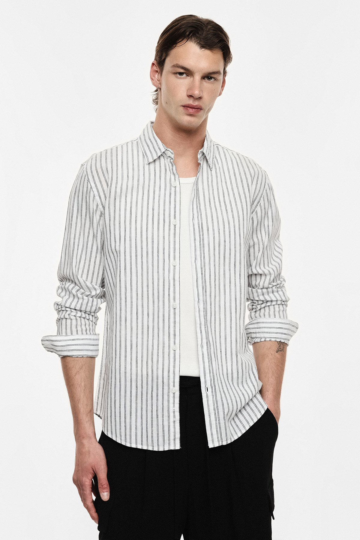 Man modelling white pinstrip shirt over white tee and black trousers against plain background