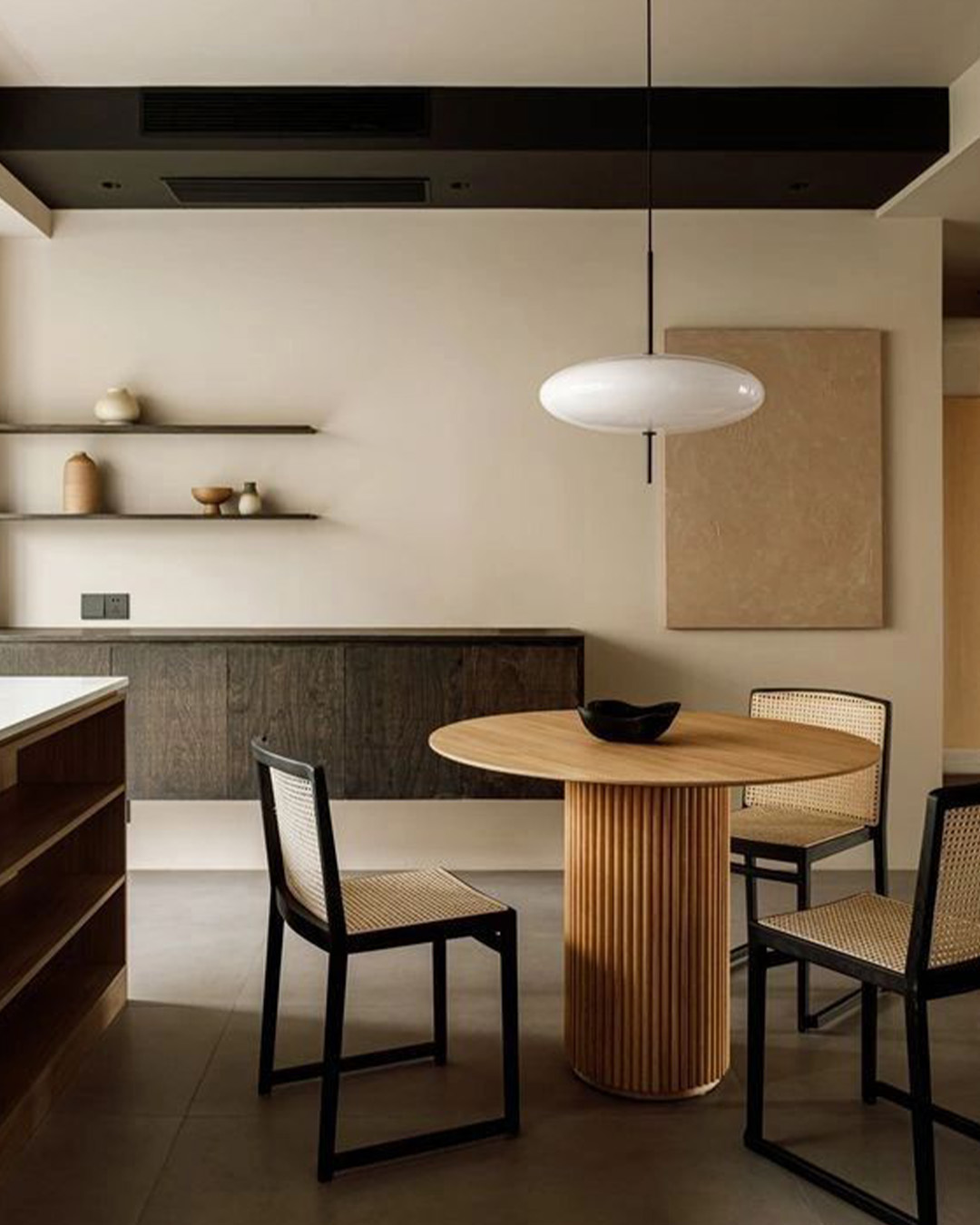 Minimalist dining room with round ribbed-wood table, cane-seat chairs, white pendant light, dark floating sideboard and neutral decor