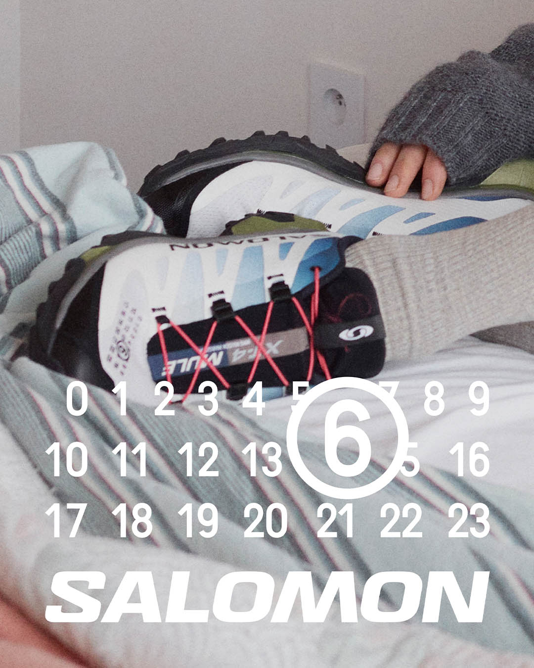 Pair of Salomon trail running shoes with red laces on a striped bed, hand resting nearby, calendar overlay showing circled 6 and SALOMON logo