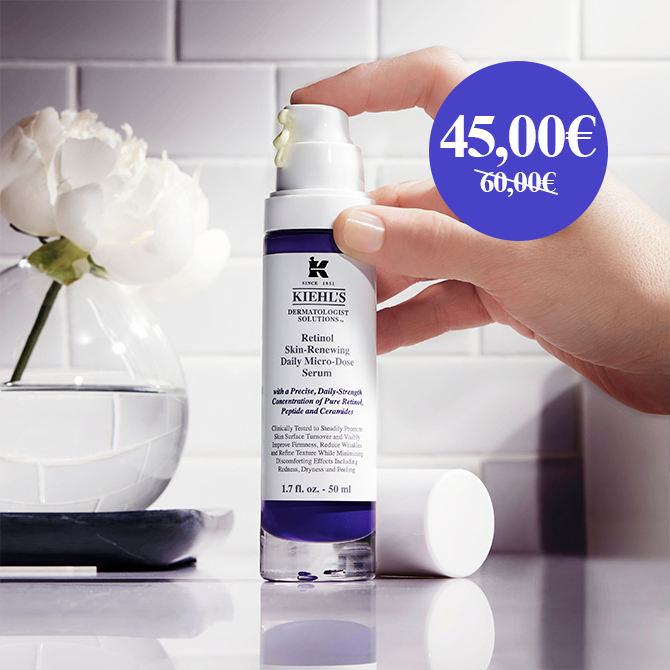 Una mano tiene il siero Retinol Daily Micro-Dose di Kiehl's davanti a un vaso di fiori bianchi
