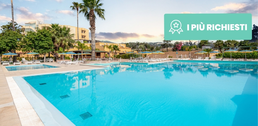 Outdoor hotel resort swimming pool with clear blue water, palm trees, sun loungers and umbrellas on a calm late afternoon