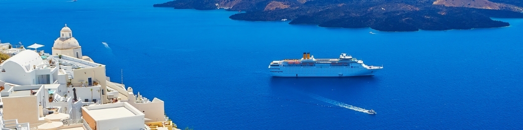Aerial view of Santorini's white cliffside buildings and blue-domed church overlooking the deep-blue caldera with a large cruise ship.
