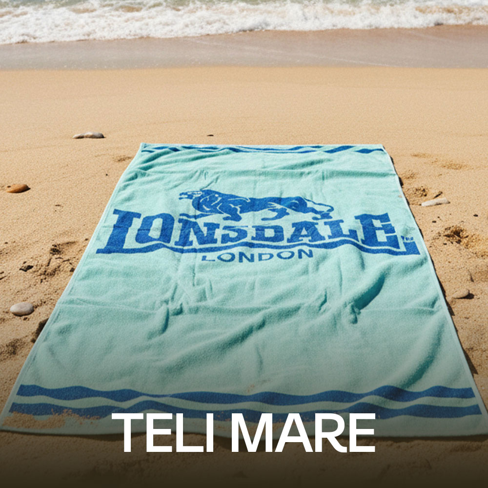 Light blue Lonsdale London beach towel laid flat on sandy shore with gentle waves in the background