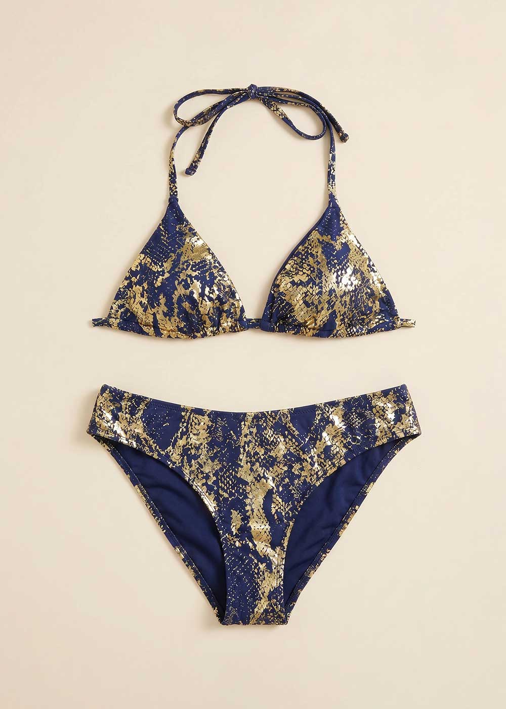 Navy and metallic gold patterned women's two-piece bikini, triangle halter top and mid-rise briefs flat-lay on cream background
