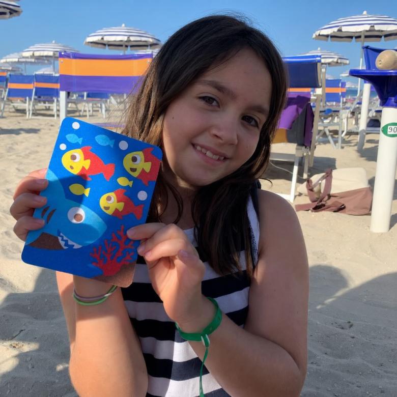 L'immagine mostra una bambina con un album Sabbiarelli in spiaggia