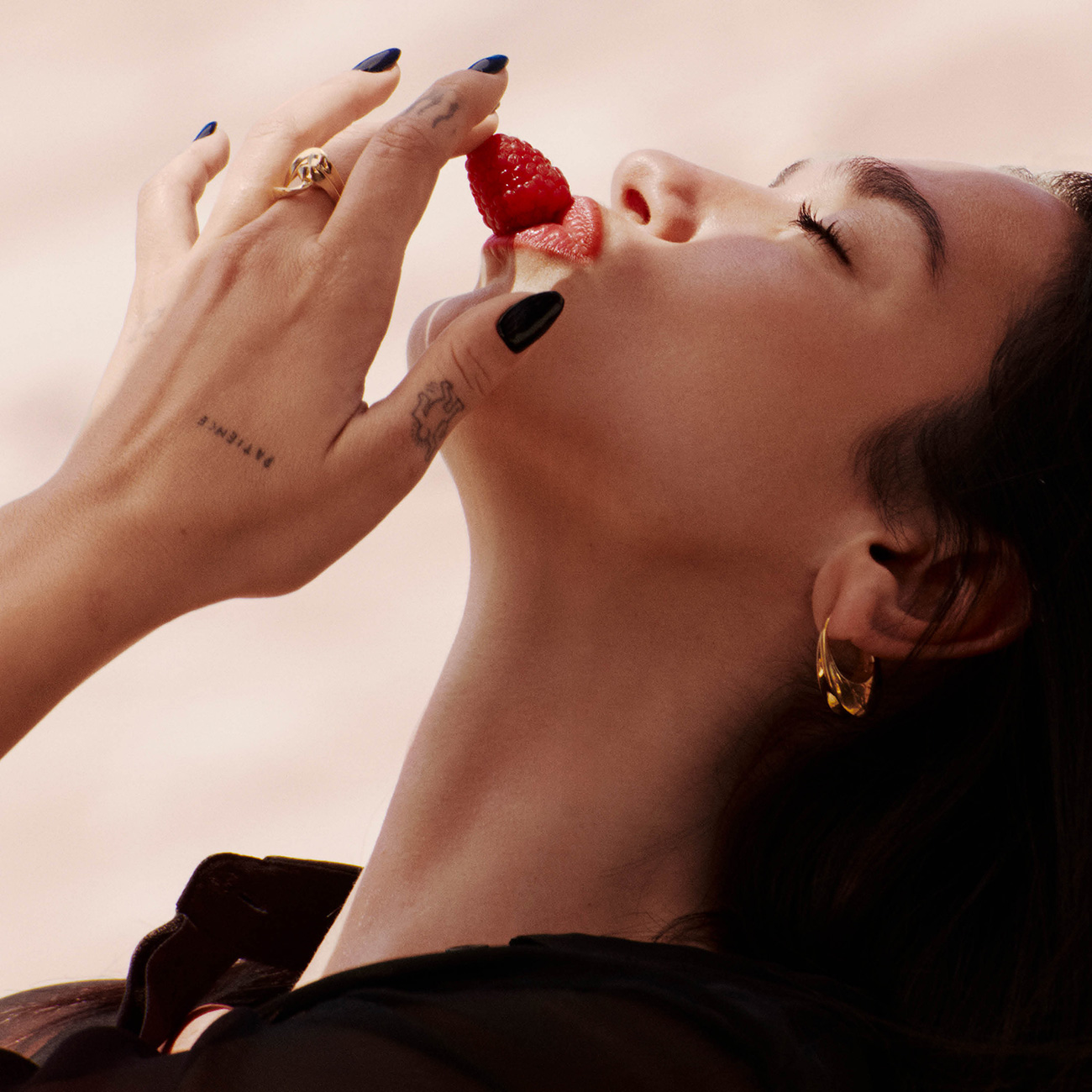 Primo piano della cantante Dua Lipa mentre posa delicatamente un lampone fresco sulle labbra rosse.
