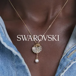 Collana con catena d'oro e ciondolo di perla a forma di conchiglia indossata su pelle scura, abbinata a una camicia di jeans azzurro chiaro.