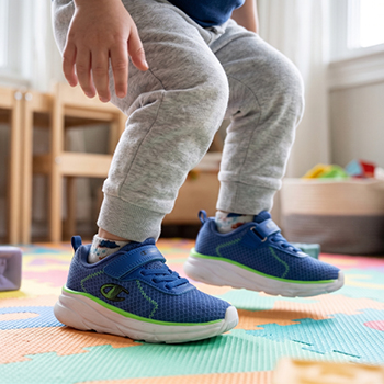 Toddler's legs and feet wearing blue mesh trainers with green trim standing on a colourful foam play mat in a bright playroom