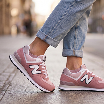 Pink New Balance trainers on a person wearing rolled-up jeans, side view on a cobbled city street