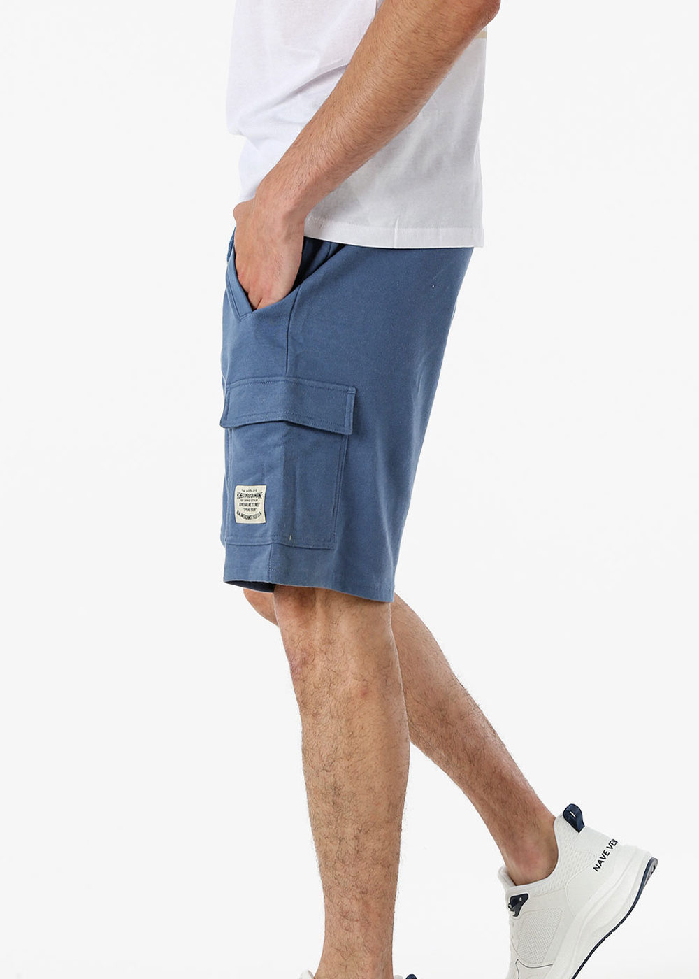 Side view of a man in a casual outfit: blue cargo shorts with flap pocket and label, white t-shirt and white trainers